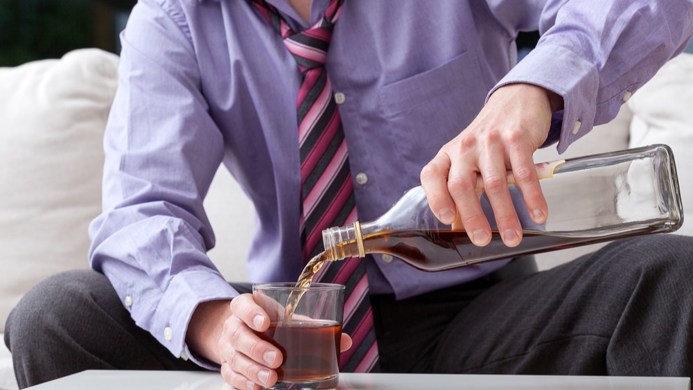 Alcohol Addiction and Abuse: Learn About Alcoholism North Jersey Recovery Center - A man sitting at home pours a glass of liquor as soon as he returns home from work as he struggles with alcohol abuse and alcoholism.