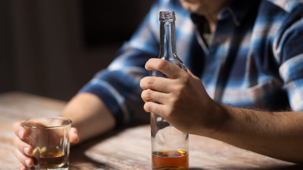 Alcohol Rehab North Jersey Recovery Center - A man is struggling with alcohol addiction to cope with stressors in life. He is debating whether or not it is the right time to seek treatment at an alcohol rehab to start his path to recovery.