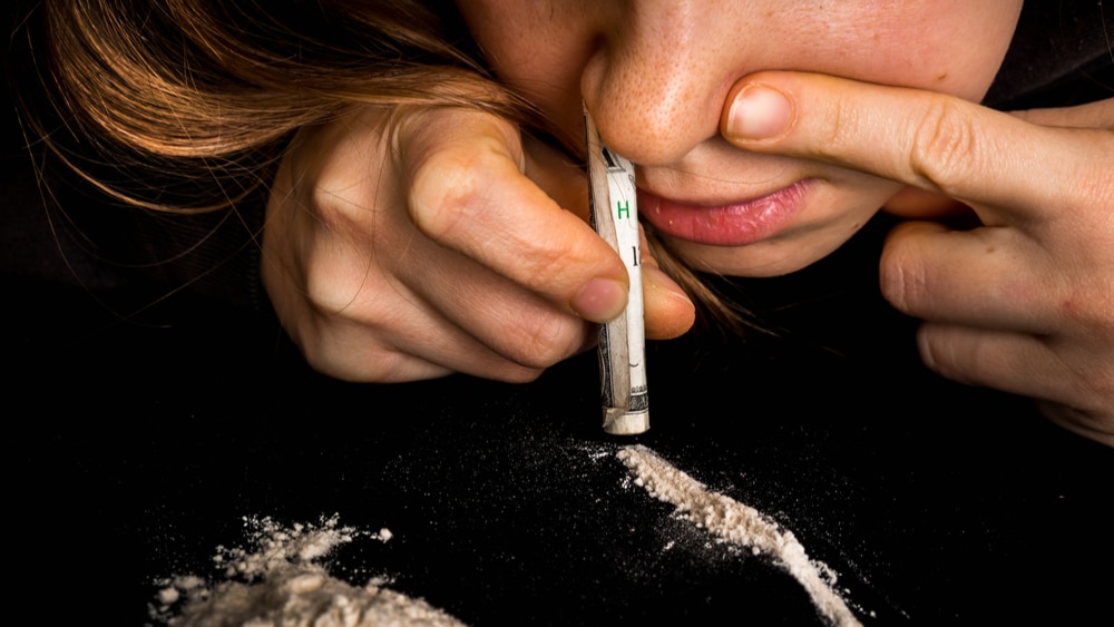 Snorting Cocaine North Jersey Recovery Center - A young woman is snorting cocaine off of a table with a dollar bill.