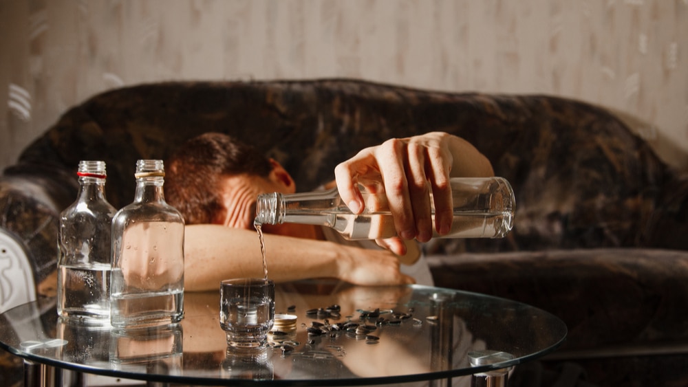 The 7 Types of Alcoholics North Jersey Recovery Center - A young male lays on his couch pouring another shot of liquor with multiple liquor bottles sitting on the living table as he debates whether he falls into the category of alcoholics and needs professional treatment.