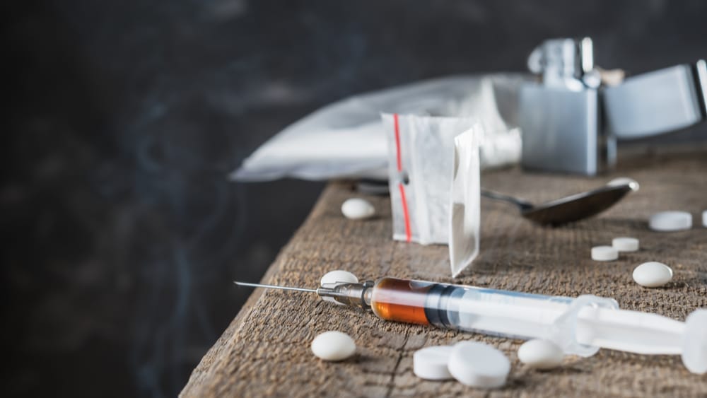 Drug Abuse and Addiction North Jersey Recovery Illicit drugs like heroin and cocaine sit next to prescription pills on a table with a needle near by.