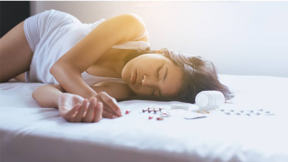 Oxycodone Withdrawal and Detox- North Jersey Recovery  - A woman lays in bed as she overdoses on oxycodone pills that lay next to her in bed.