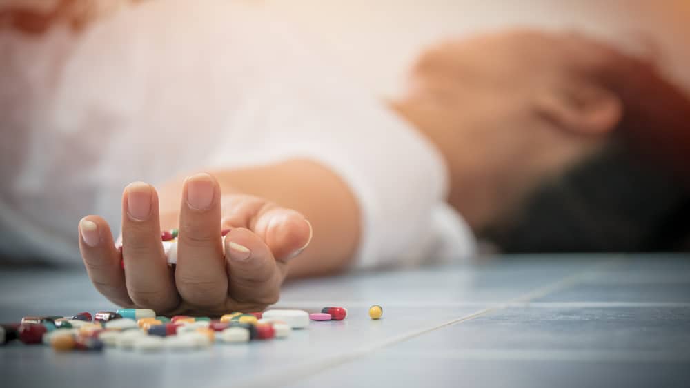 The Opioid Epidemic - North Jersey Recovery - A man lays on the ground with his arm out towards a pile of pills.