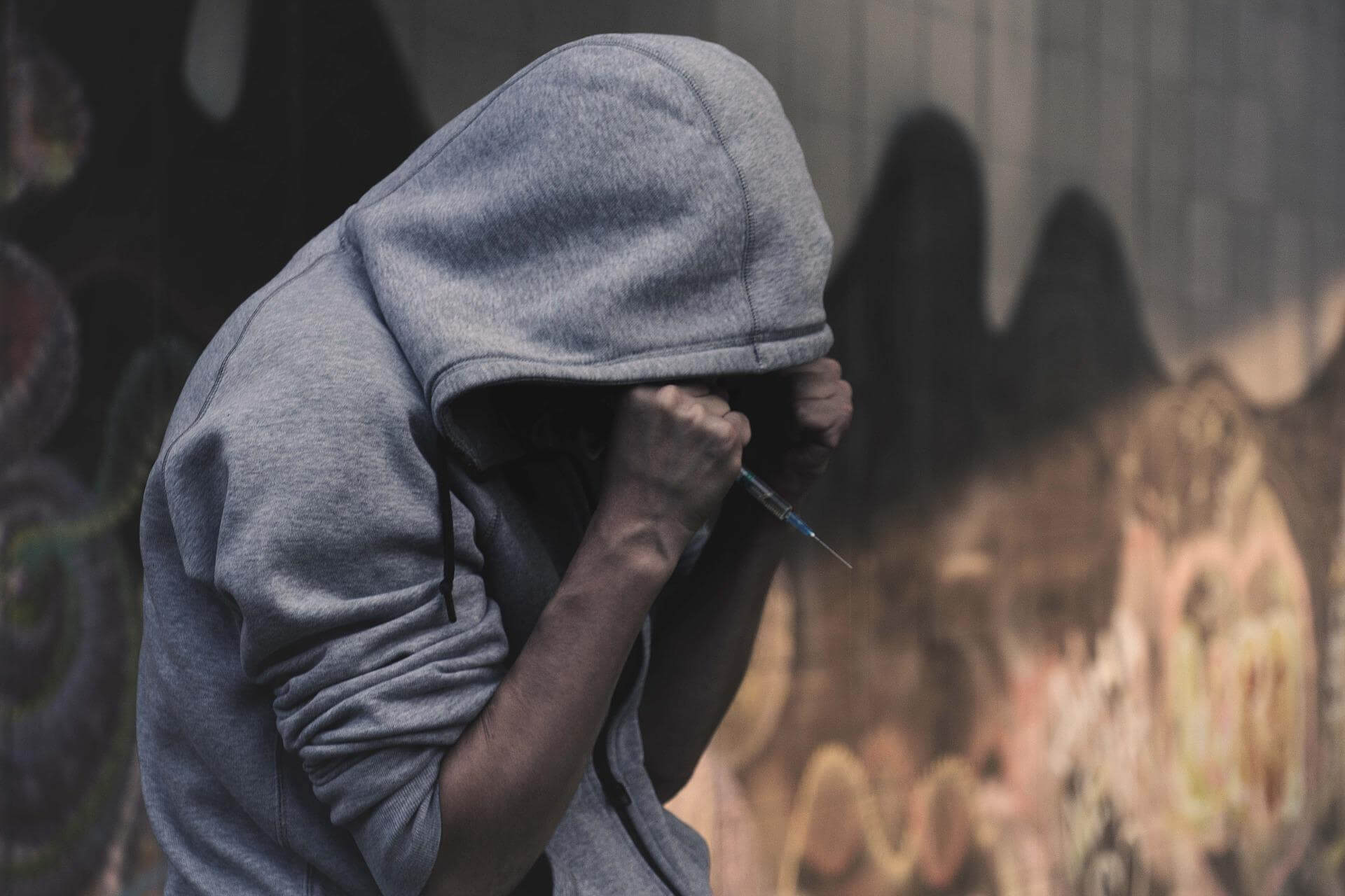 Person with hoodie holding drug syringe
