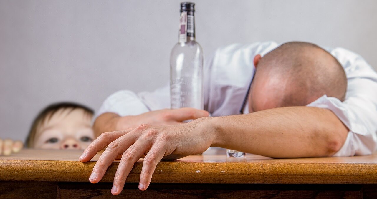 Dad slumped over on desk with alcohol bottle and son watching - Drinking In Private