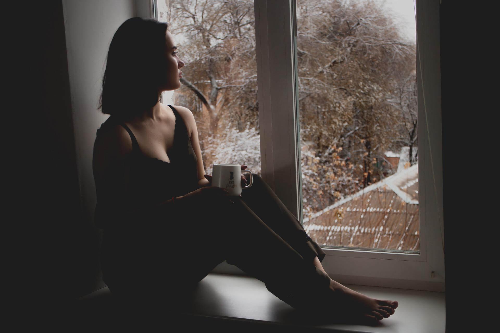 Girl in dark room looking out window - spouse suffering from addiction
