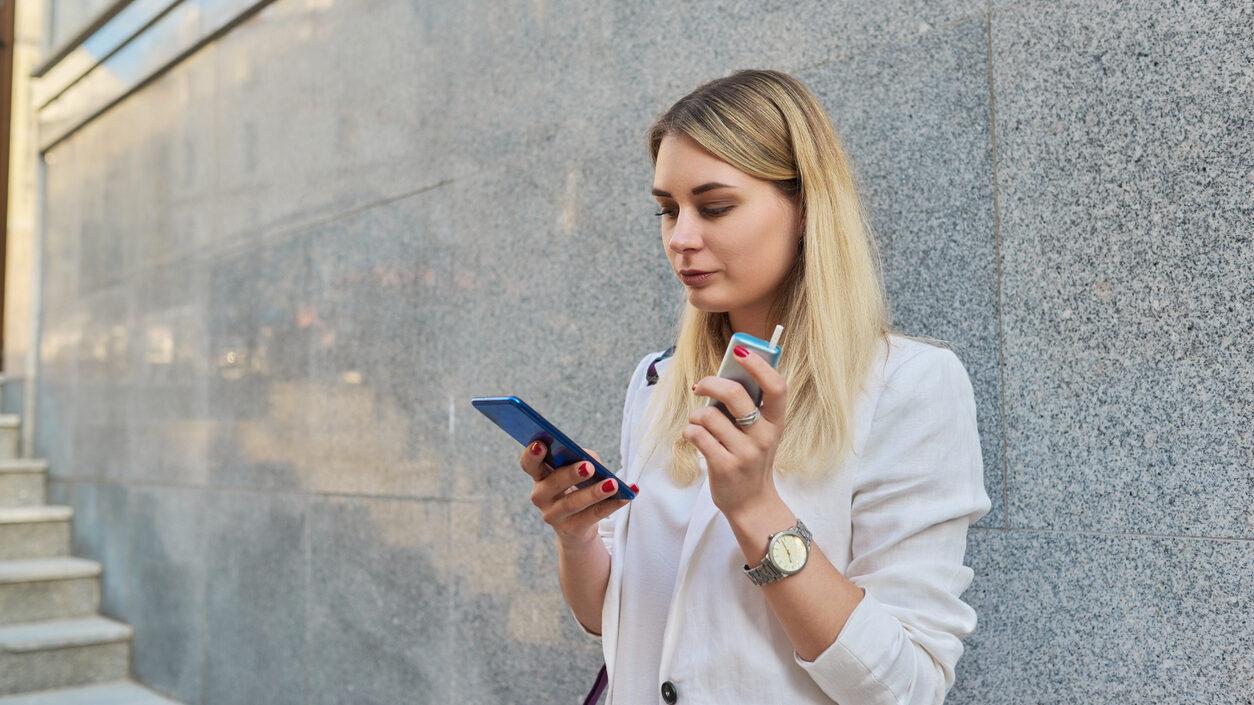 Nicotine Addiction Affects Work - young woman with smartphone resting smoking electronic cigarette, tobacco product