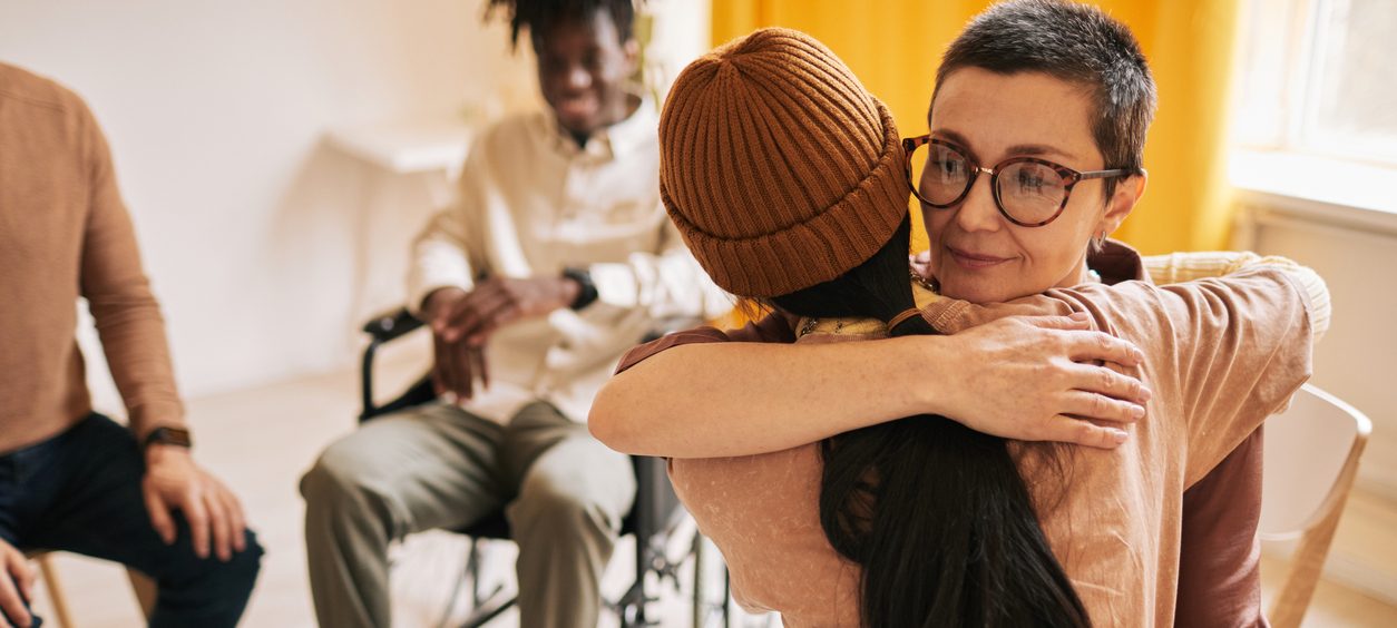 Two women hugging in support in group therapy